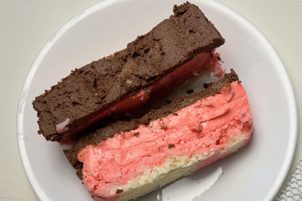 Two slices of layered cake on a plate, one with chocolate frosting and the other with pink frosting. A fork rests on a folded white napkin in the background.