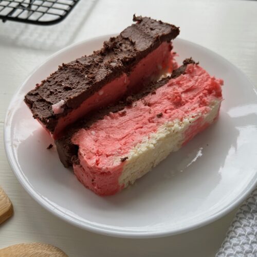 Two slices of layered cake with chocolate and pink frosting on a white plate.