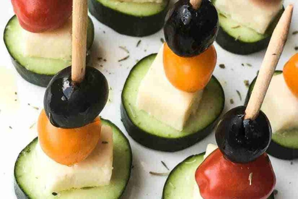 Appetizers with skewers of black olives, cherry tomatoes, and cheese cubes on cucumber slices.