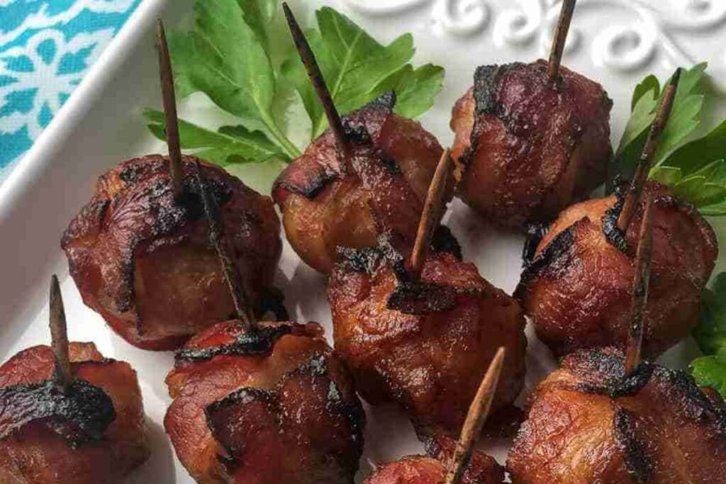 Bacon-wrapped appetizers secured with toothpicks on a white plate, garnished with fresh parsley.