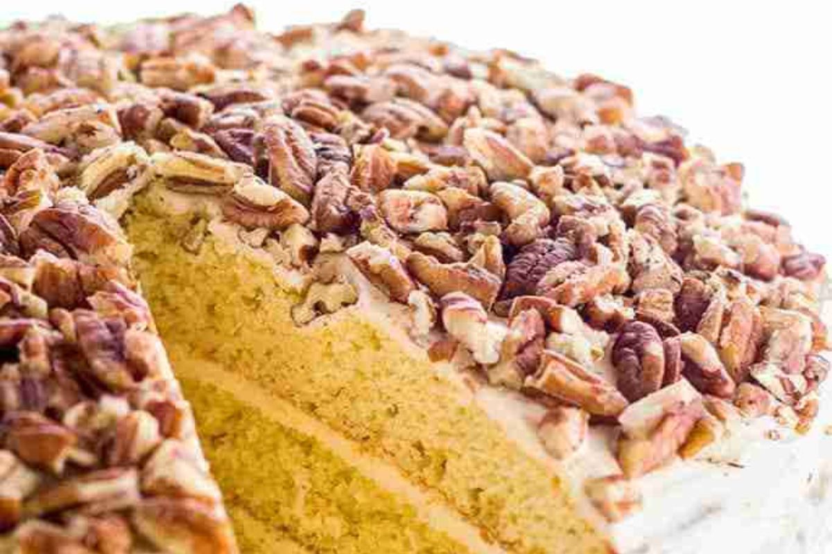A sliced layered cake topped with chopped pecans, revealing moist yellow sponge layers inside.