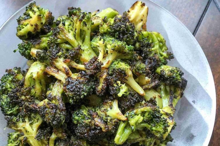 A bowl of blackened broccoli florets with charred edges, served on a glass plate.