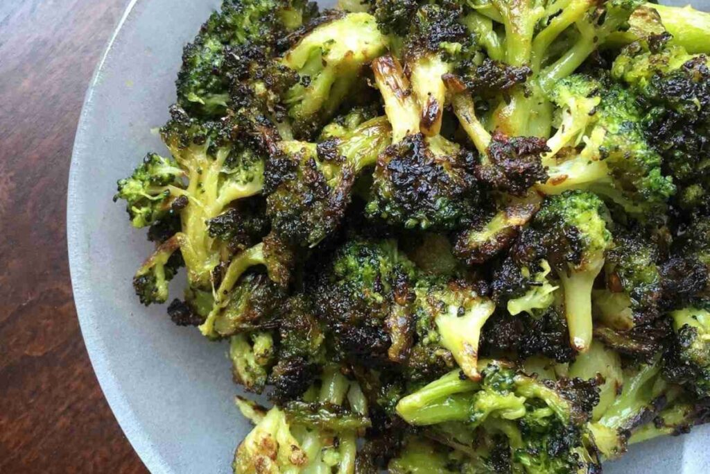A plate of blackened broccoli florets with browned, crispy edges arranged on a light-colored dish.