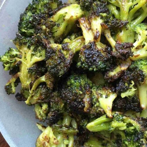 A plate of blackened broccoli florets with browned, crispy edges arranged on a light-colored dish.