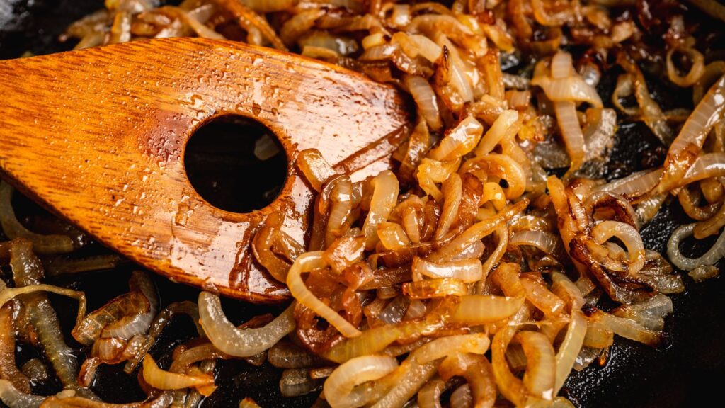 Caramelized onions being stirred in a pan with a wooden spatula.