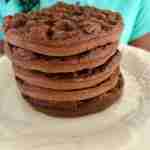 A stack of four chocolate waffles on a white plate.