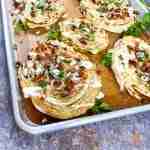 Roasted cabbage steaks on a baking sheet topped with blue cheese, bacon bits, and parsley.