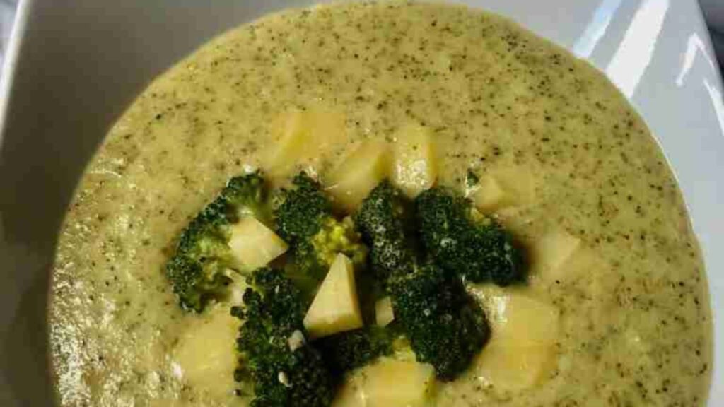Bowl of broccoli and cheese soup with broccoli florets and cheese cubes on top.