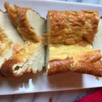 A keto egg loaf with a golden-brown crust, sliced into three large pieces on a white rectangular plate.