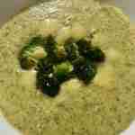 A bowl of creamy broccoli soup with broccoli florets and cheese pieces on top.