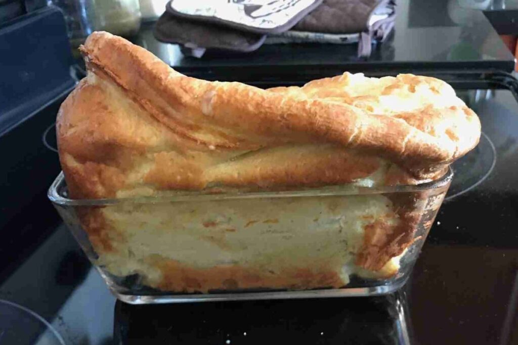A loaf of bread with a puffy top is in a glass baking dish on a stovetop.