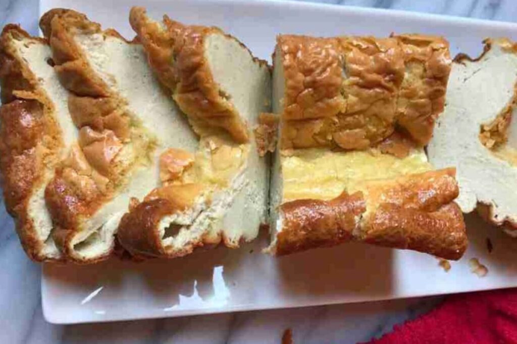 Sliced loaf of bread on a rectangular white plate with a red cloth nearby.