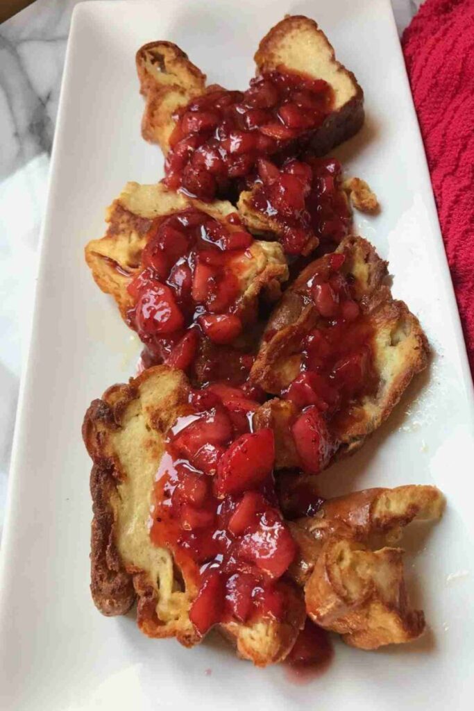 French toast pieces topped with strawberry compote on a rectangular white plate.