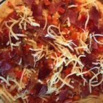 A homemade pizza topped with cheese, pepperoni slices, and diced red bell peppers on a thin crust.