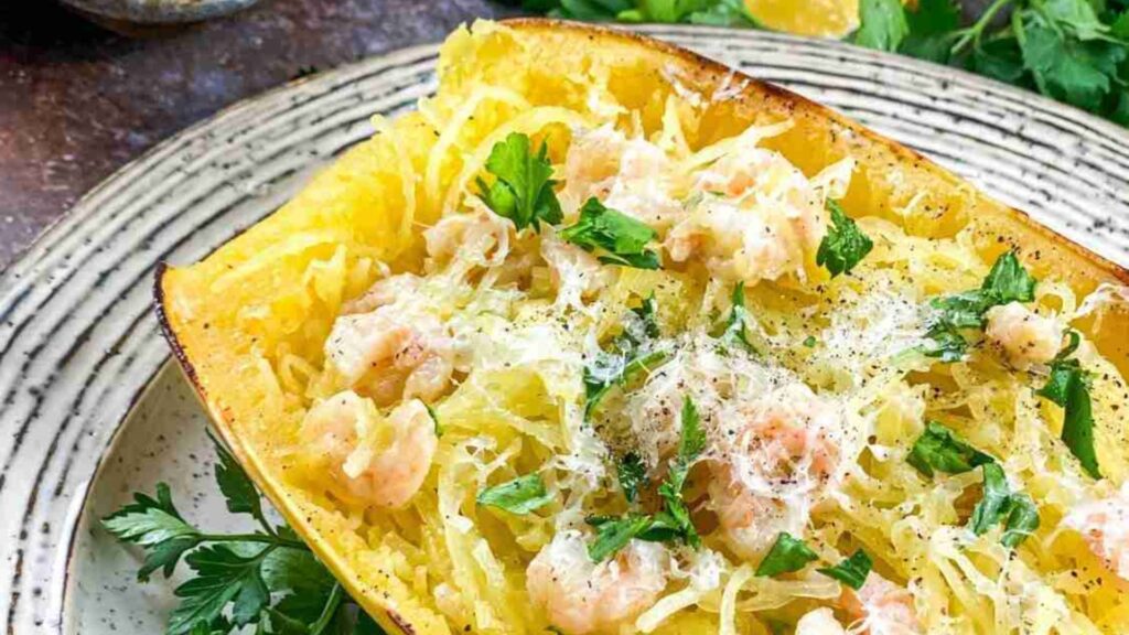 A halved spaghetti squash filled with shrimp scampi, grated cheese, and parsley rests elegantly on a white plate.