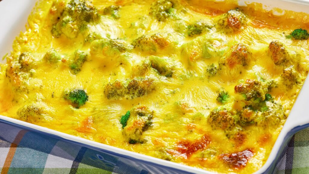 A baked casserole dish with melted cheese and broccoli on top, resting on a checkered tablecloth.