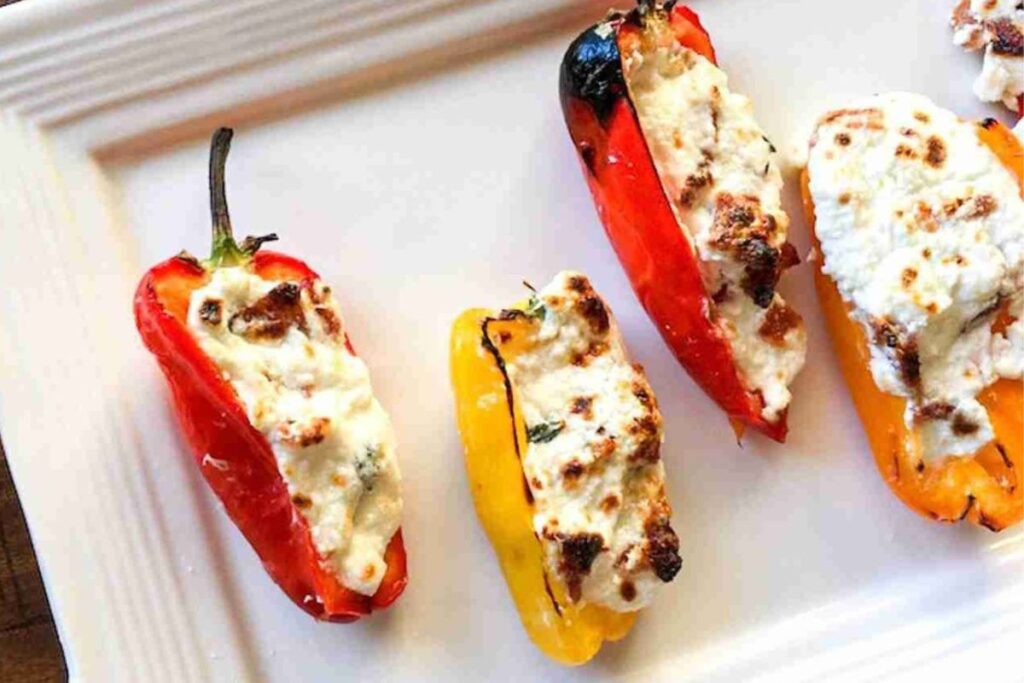 Four grilled stuffed peppers with a creamy topping are arranged on a white rectangular plate.