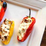 Three stuffed peppers with melted cheese filling are arranged on a white square plate.