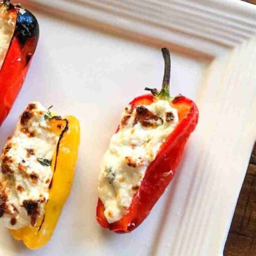 Three stuffed peppers with melted cheese filling are arranged on a white square plate.
