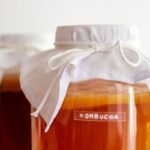 Two glass jars covered with cloths are filled with kombucha, a fermented tea drink.