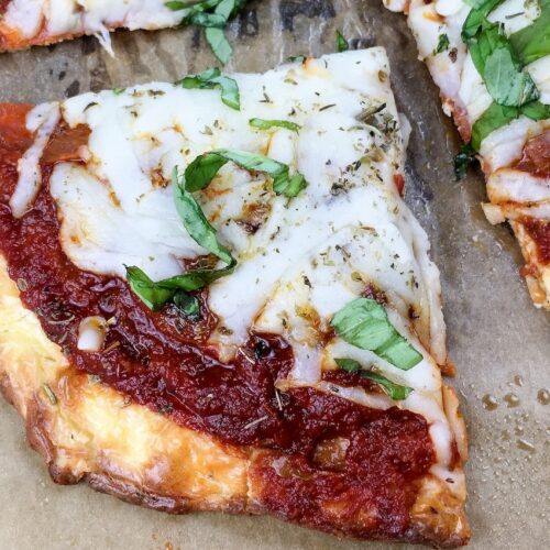 A slice of pizza with melted cheese, tomato sauce, and fresh basil on a parchment paper background.