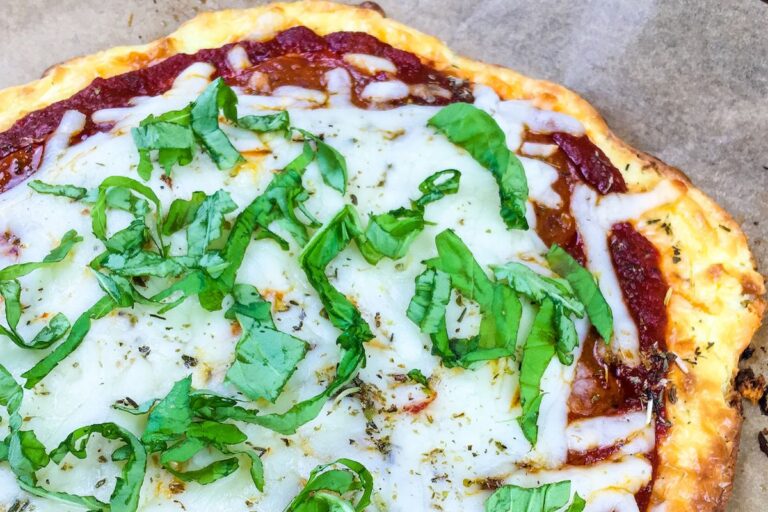 Cheese pizza topped with tomato sauce, melted cheese, and fresh basil on a parchment paper background.
