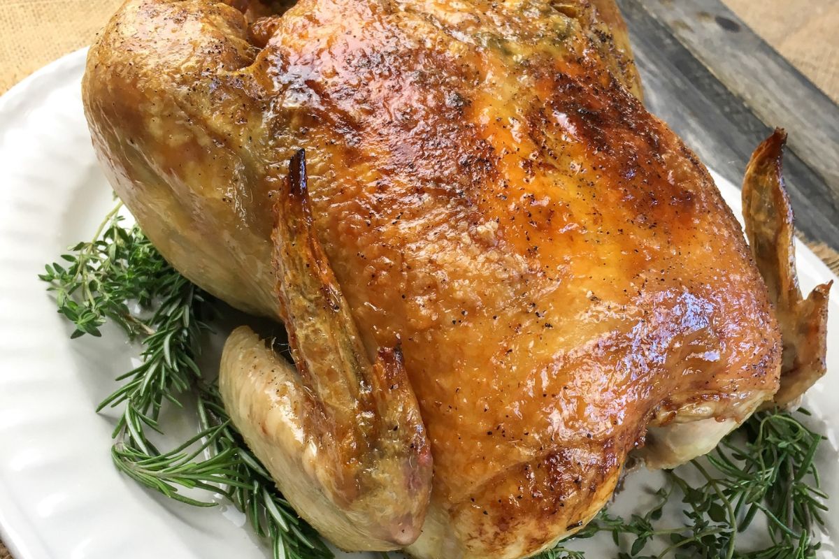 Golden-brown roasted chicken on a white plate garnished with fresh herbs.