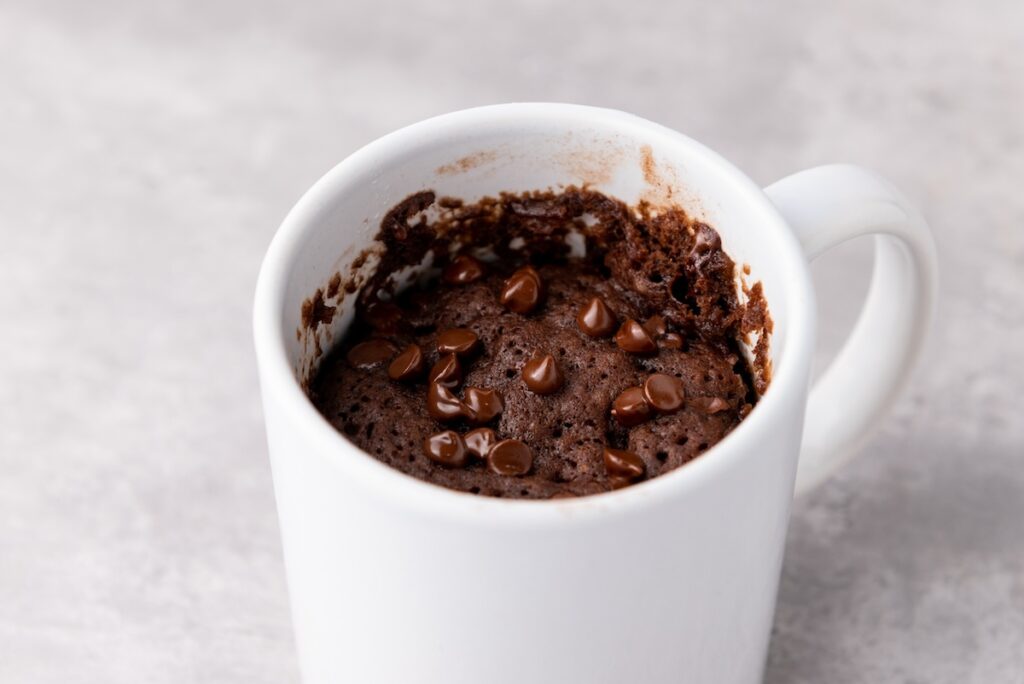 A white mug containing a chocolate mug cake topped with chocolate chips on a light gray surface.
