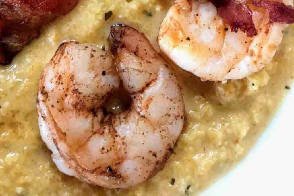 Close-up of grilled shrimp on a bed of creamy grits, garnished with crispy bacon.