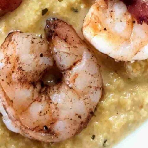 Close-up of grilled shrimp on a bed of creamy grits, garnished with crispy bacon.