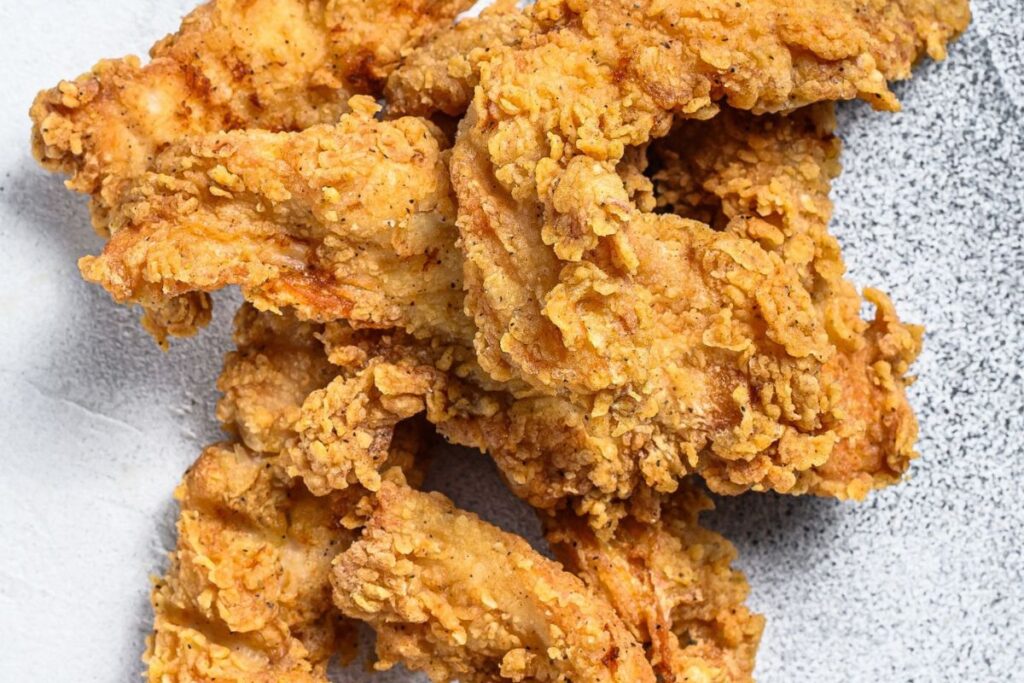 Close-up of golden-brown fried chicken tenders on a speckled gray surface.