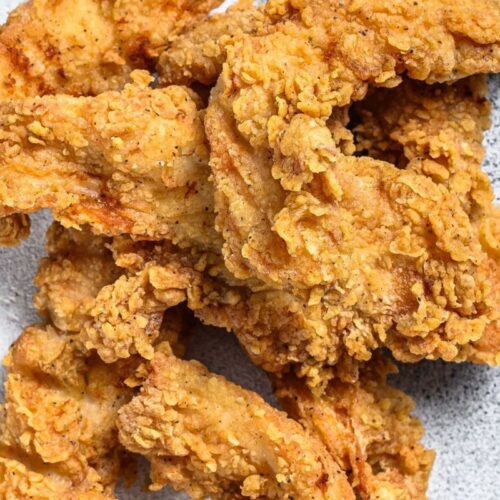 Close-up of golden-brown fried chicken tenders on a speckled gray surface.