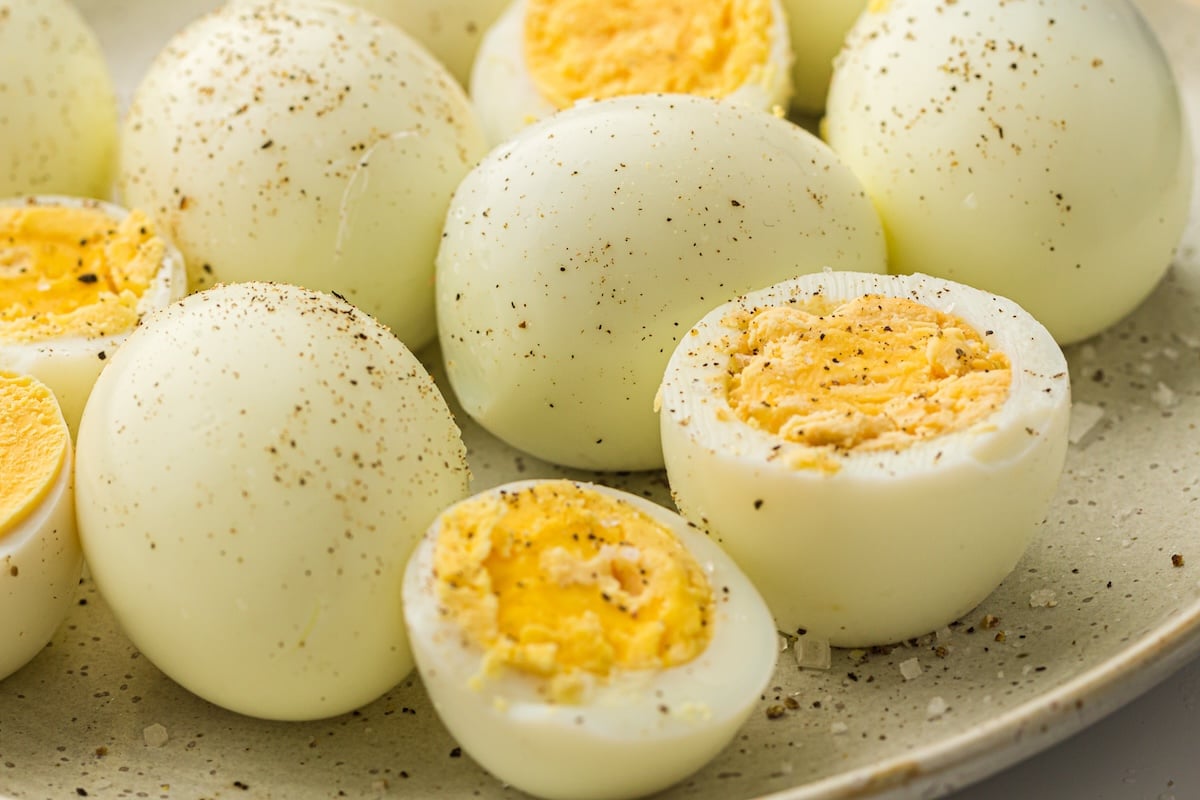 Peeled hard-boiled eggs seasoned with black pepper and salt on a plate.