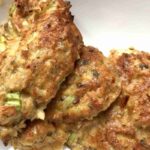 Close-up of three cooked, golden-brown patties with visible herbs and green bits, on a white plate.
