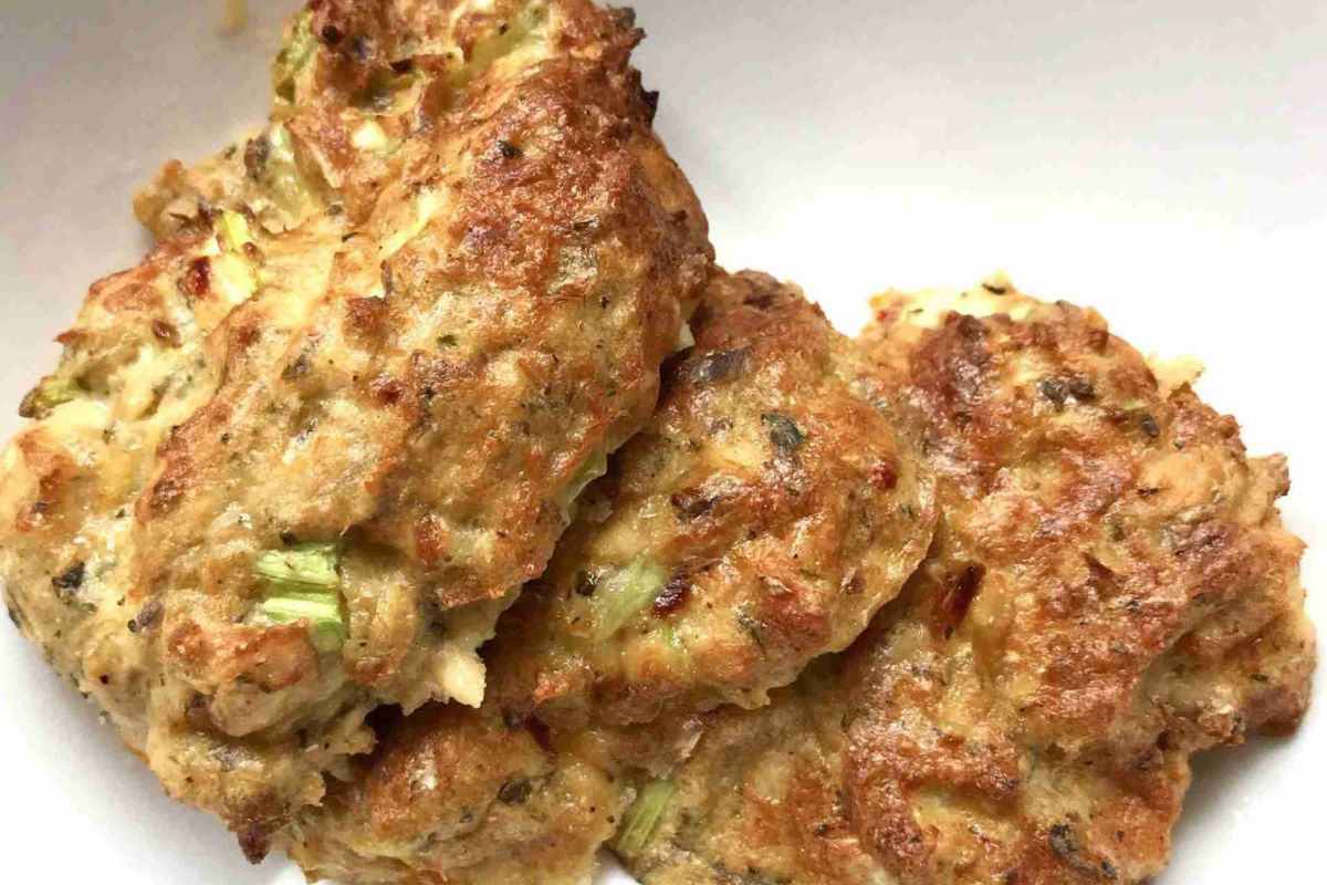 Close-up of three cooked, golden-brown patties with visible herbs and green bits, on a white plate.