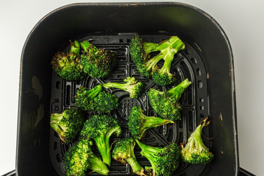 Broccoli florets cooked in an air fryer, placed in a black basket on a white surface.
