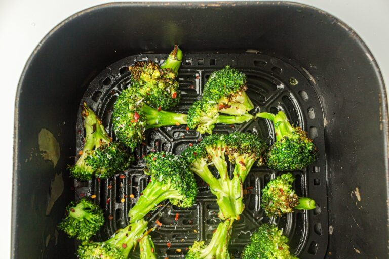 Cooked broccoli florets in an air fryer basket, lightly charred with visible seasoning specks.