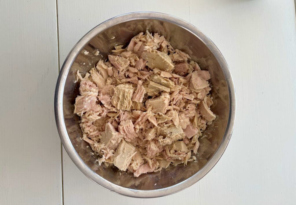 A metal bowl filled with succulent chunks of canned tuna rests on a pristine white surface.