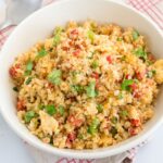 A bowl of cauliflower rice mixed with diced vegetables and garnished with cilantro, placed on a red and white checkered cloth with a spoon nearby.