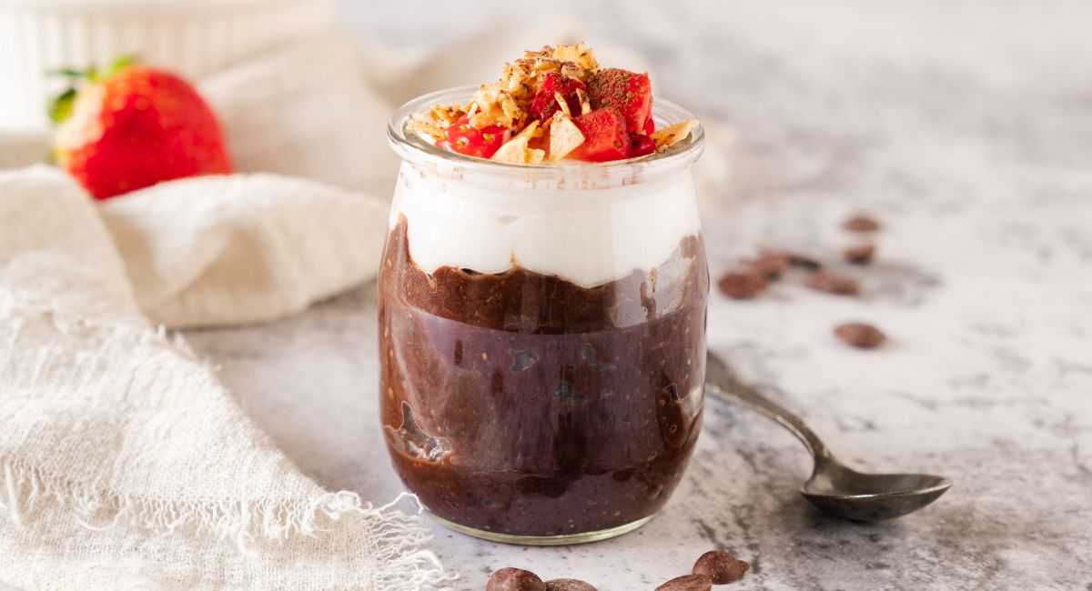 A clear glass of chocolate chia mousse topped with strawberry bits.