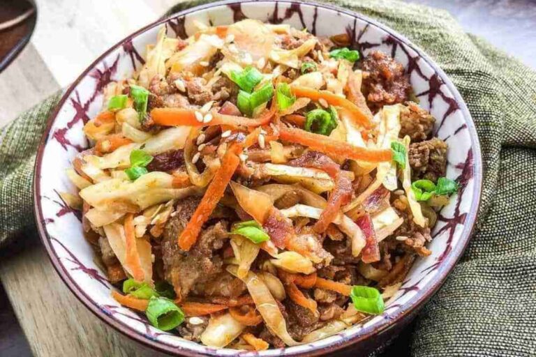 A bowl of stir-fried vegetables and meat, reminiscent of a deconstructed sausage egg roll, featuring carrots, cabbage, and green onions, elegantly presented on a patterned dish.