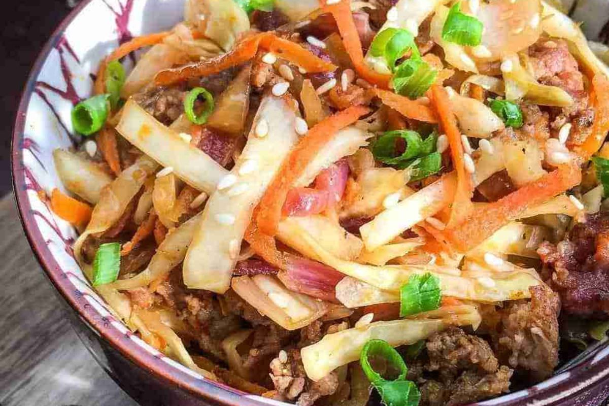 A savory bowl of stir-fried vegetables with carrots, cabbage, and scallions, lightly garnished with sesame seeds—reminiscent of the flavors found in a delicious sausage egg roll.