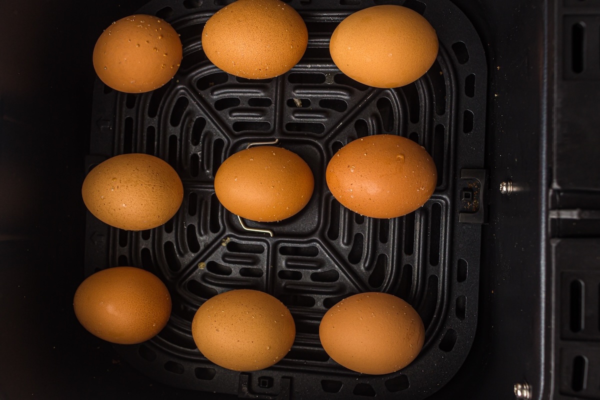 Nine brown eggs arranged on a black tray.