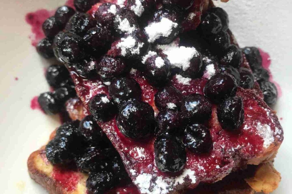 Waffles topped with a generous amount of blueberries and a dusting of powdered sugar.