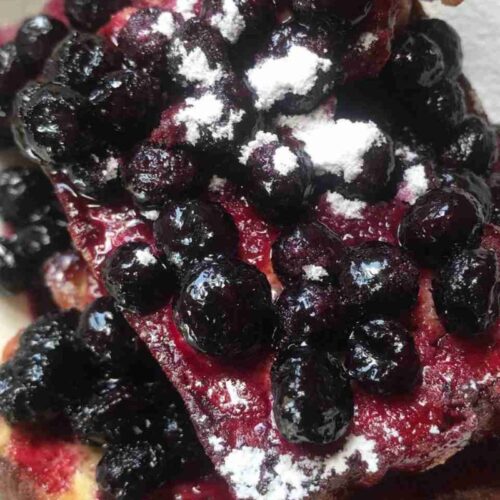 Waffles topped with a generous amount of blueberries and a dusting of powdered sugar.