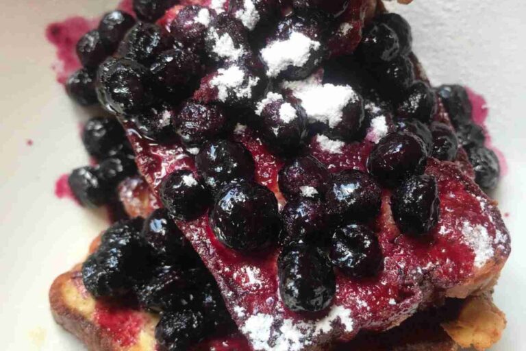 Waffles topped with a generous amount of blueberries and a dusting of powdered sugar.