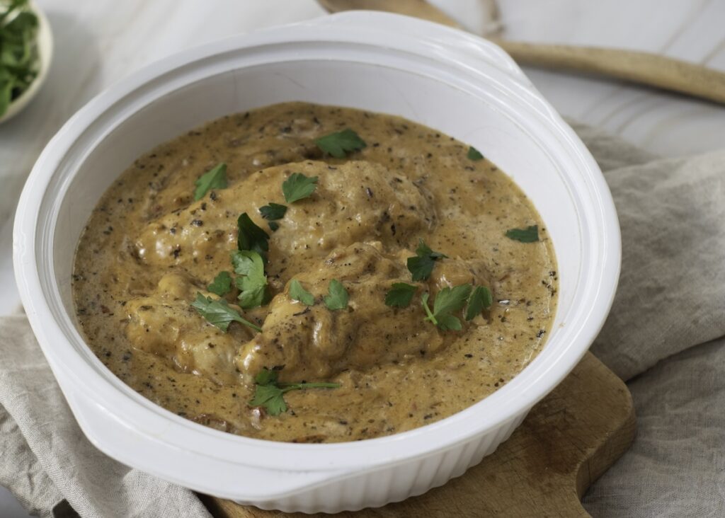 A white ceramic dish with low carb, creamy mushroom gravy garnished with parsley, sits invitingly on a wooden board, reminiscent of the irresistible allure of marry me chicken.