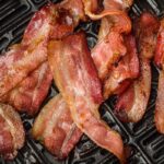 Crispy cooked bacon strips lie on a dark non-stick grill pan surface.