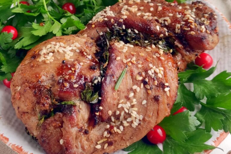 Grilled pork tenderloin garnished with sesame seeds and herbs, surrounded by fresh parsley and small red berries on a plate. Perfectly cooked in an air fryer for a succulent taste.