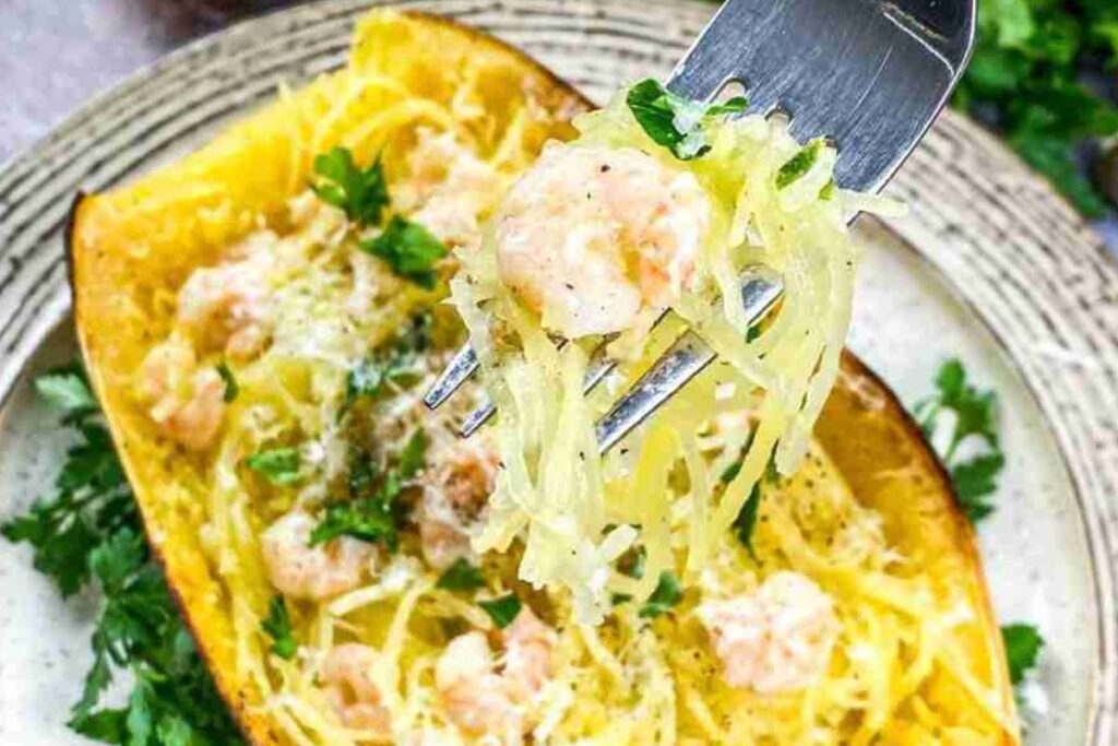 Fork with shrimp scampi, spaghetti squash, and parsley nestled over a spaghetti squash boat on a plate.